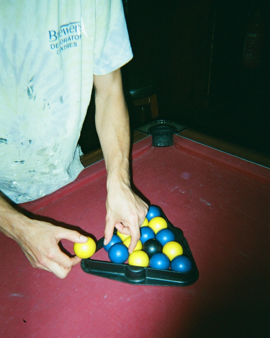 Photograph of someone's hands racking up pool balls on a red pool table
